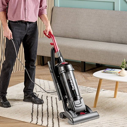 Person using a Sanitaire vacuum cleaner on a rug in a living room.