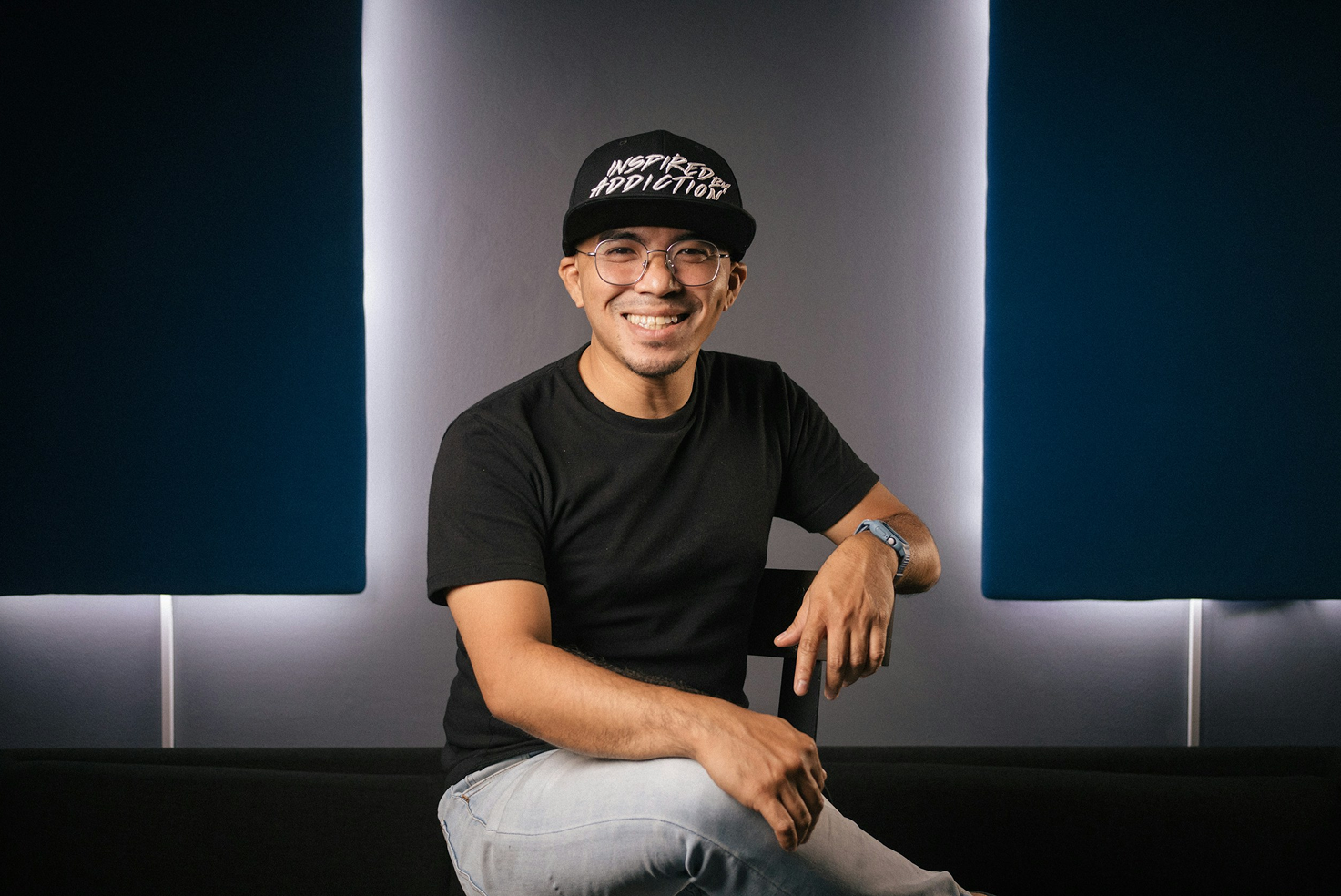 Man wearing a black cap and black t-shirt sitting against a modern interior background