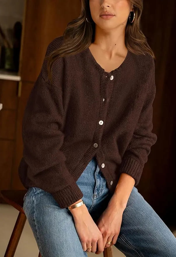 Woman wearing a brown cardigan and blue jeans sitting indoors.