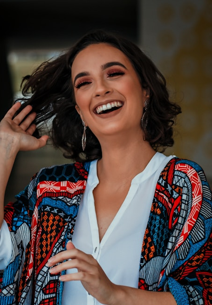 Woman wearing a colorful patterned jacket over a white shirt, smiling outdoors.