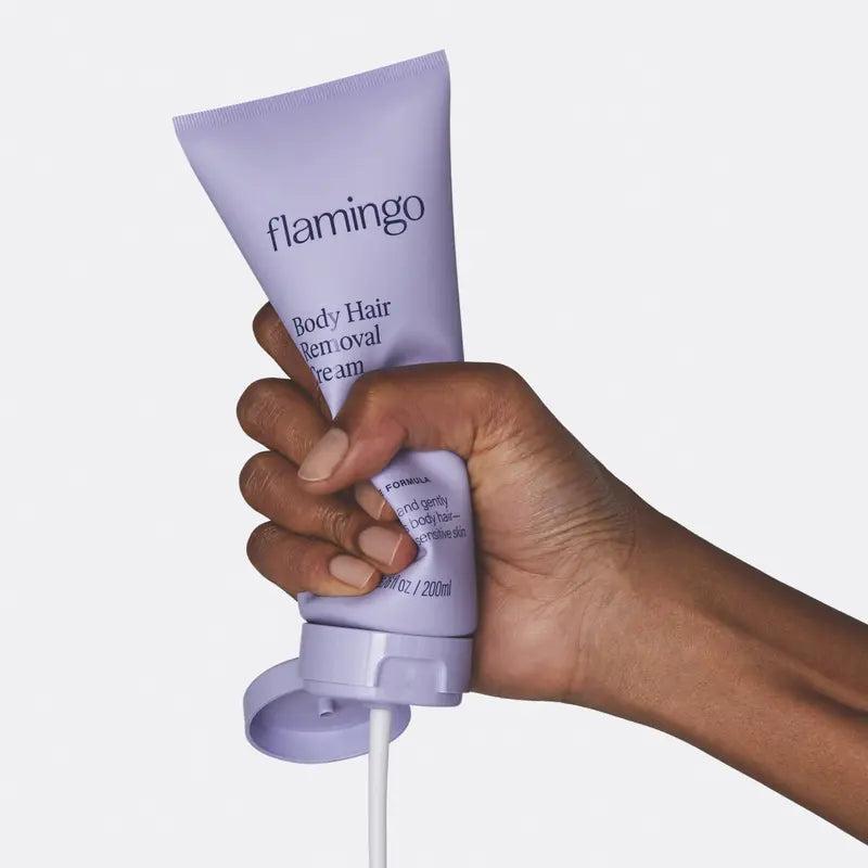 Hand holding a purple 'flamingo' body hair removal cream tube against a white background