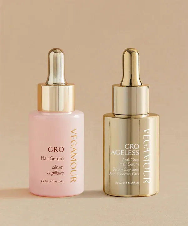 Two Vegamour hair serum bottles, one pink and one gold, on a beige background.
