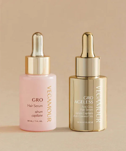 Two Vegamour hair serum bottles, one pink and one gold, on a beige background.