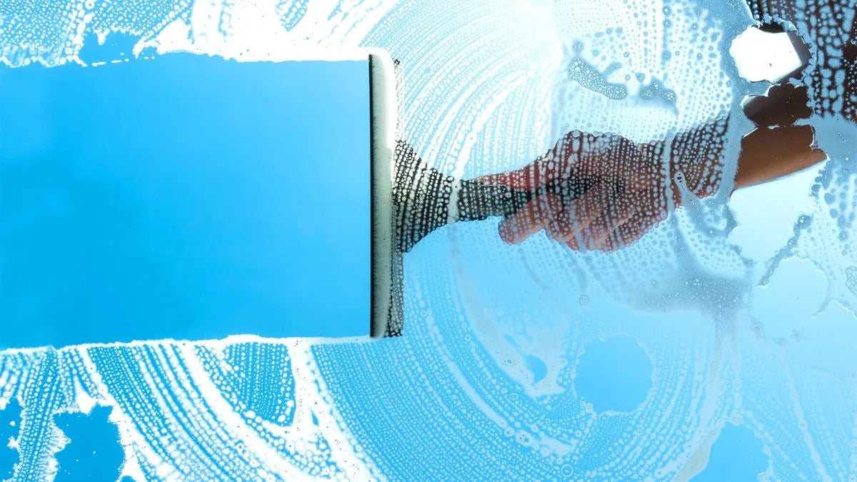 Squeegee cleaning a window with soap suds on a blue background
