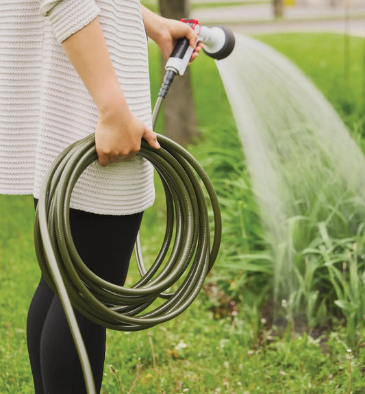 Person holding a garden hose spraying water on grass