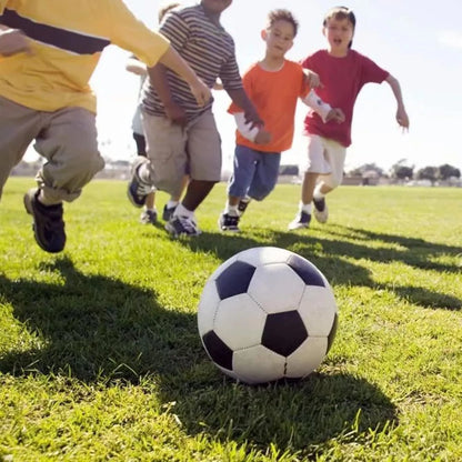 Children playing soccer on a grass field with a clear sky.