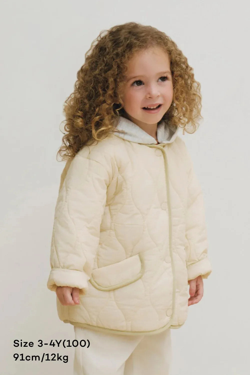 Child wearing a cream quilted jacket on a plain background