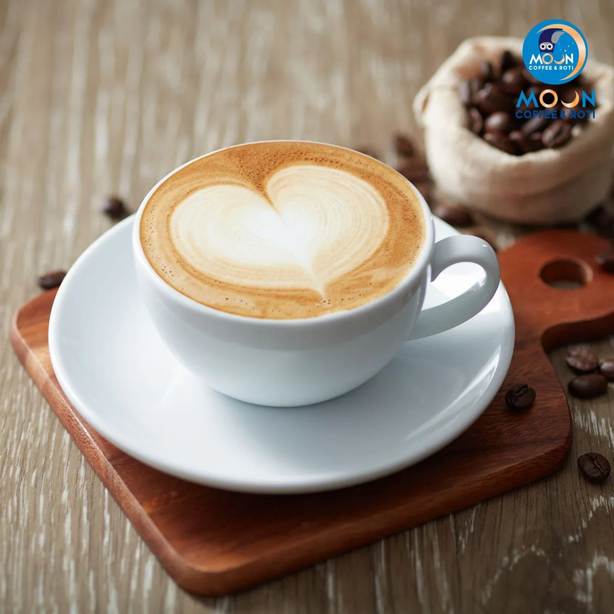Latte with heart foam in a white cup on a wooden tray, Moon Coffee Roasters logo visible.