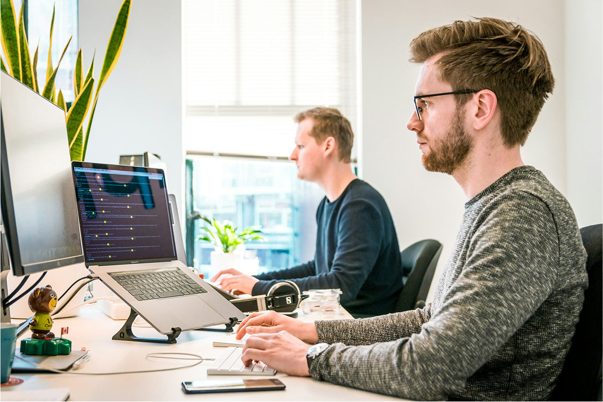 Two individuals working at a desk with computers in an office setting.