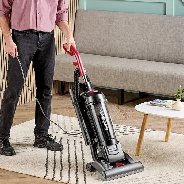 Person using a Sanitaire vacuum cleaner on a rug in a living room.