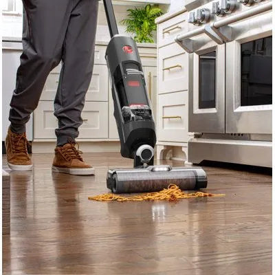 Person using a vacuum cleaner on a wooden floor in a kitchen.